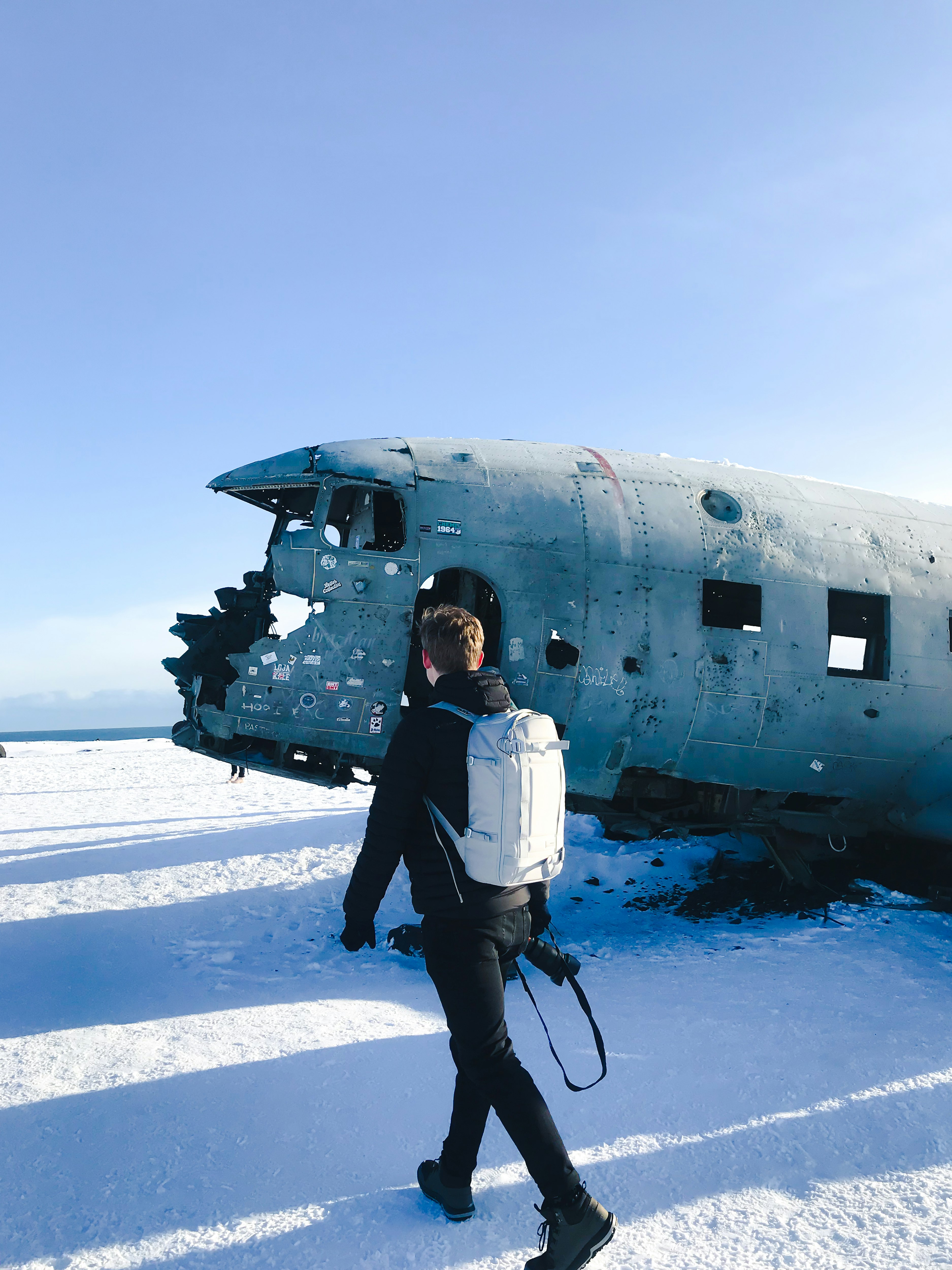 man in white jacket and black pants standing on snow covered ground near white airplane during